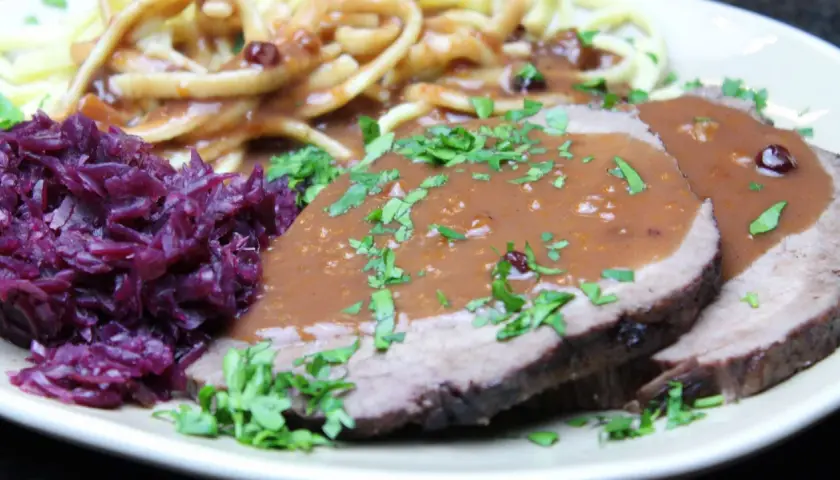 Sauerbraten einlegen rotwein: zarte Scheiben Fleisch in dunkler Soße, dazu Rotkohl und Nudeln.