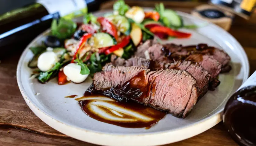 Saftiges Roastbeef als Beilage mit einem frischen Salat aus Tomaten, Gurken, Paprika und Mozzarella-Kugeln, beträufelt mit dunkler Sauce.