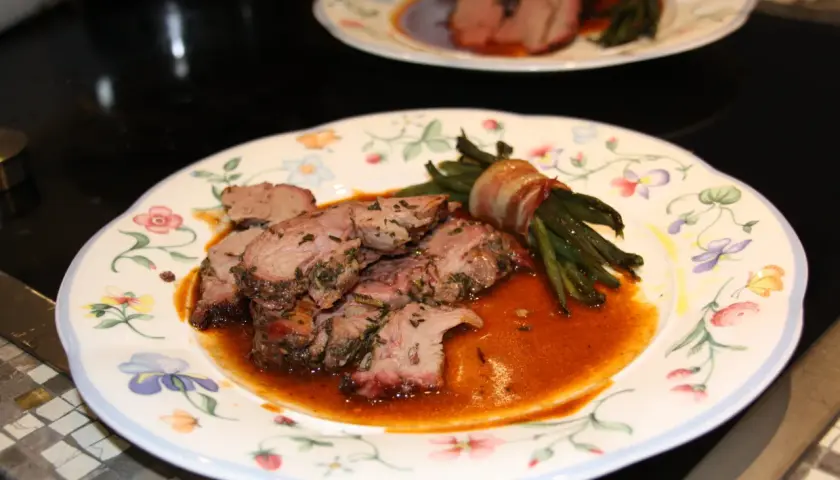 Zarte Lammfleischscheiben mit Kräutern, serviert mit Speck-umwickelten grünen Bohnen und einer köstlichen Sauce zu Lamm.