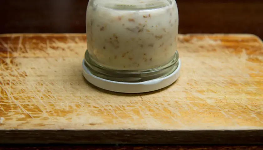 Glas mit Griebenschmalz, bereit für das Griebenschmalz Rezept. Auf einem Holzbrett.