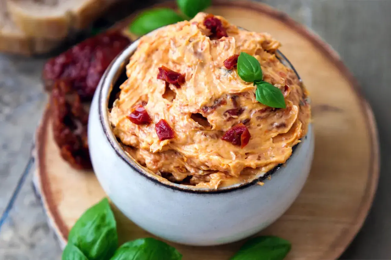 Cremige Tomatenbutter selbst machen: Ein Schälchen mit köstlicher Tomatenbutter, garniert mit Basilikum und getrockneten Tomatenstücken.