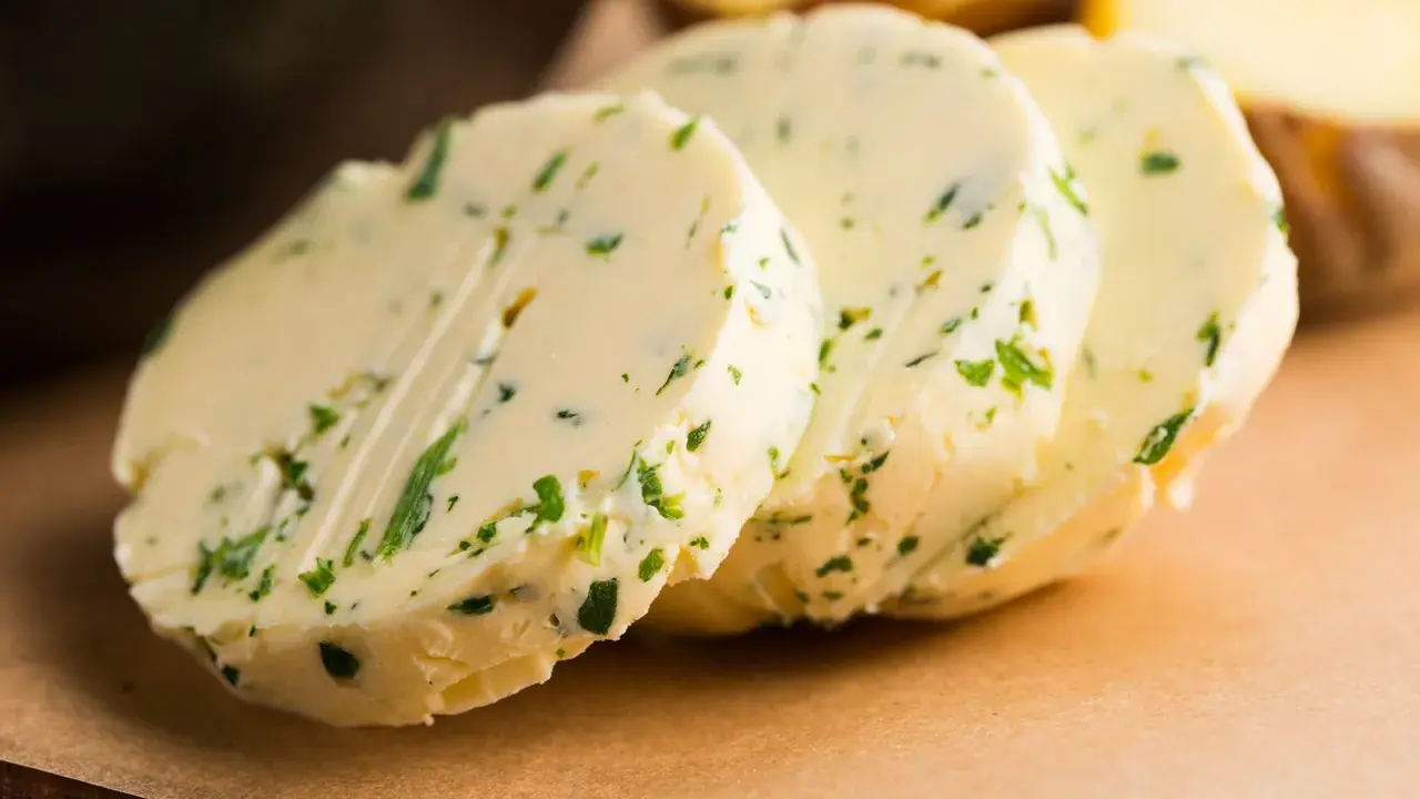 Drei Scheiben Kapuzinerkressebutter liegen auf einem braunen Untergrund. Die Butter ist mit grünen Kräutern durchsetzt.