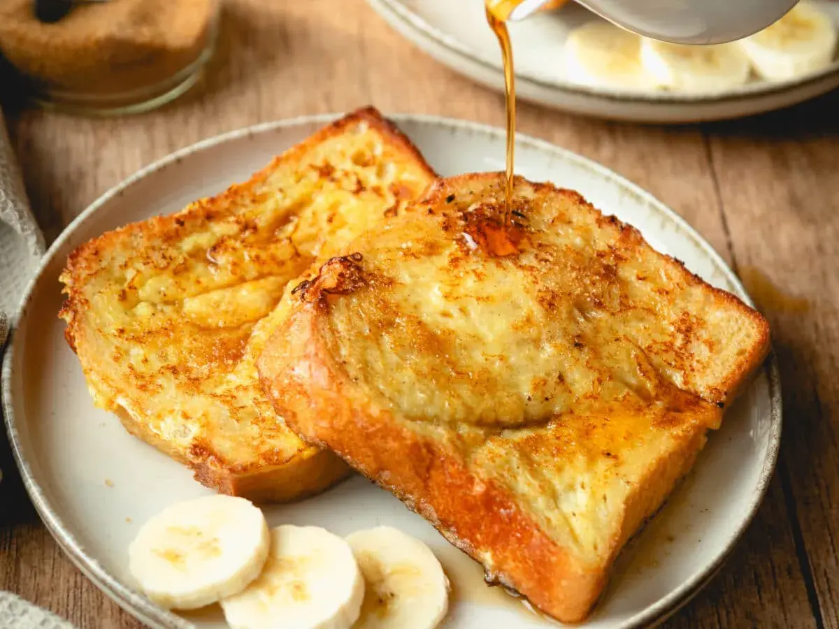 Arme Ritter, goldbraun gebraten, werden mit Sirup übergossen. Dazu Bananenscheiben und brauner Zucker.