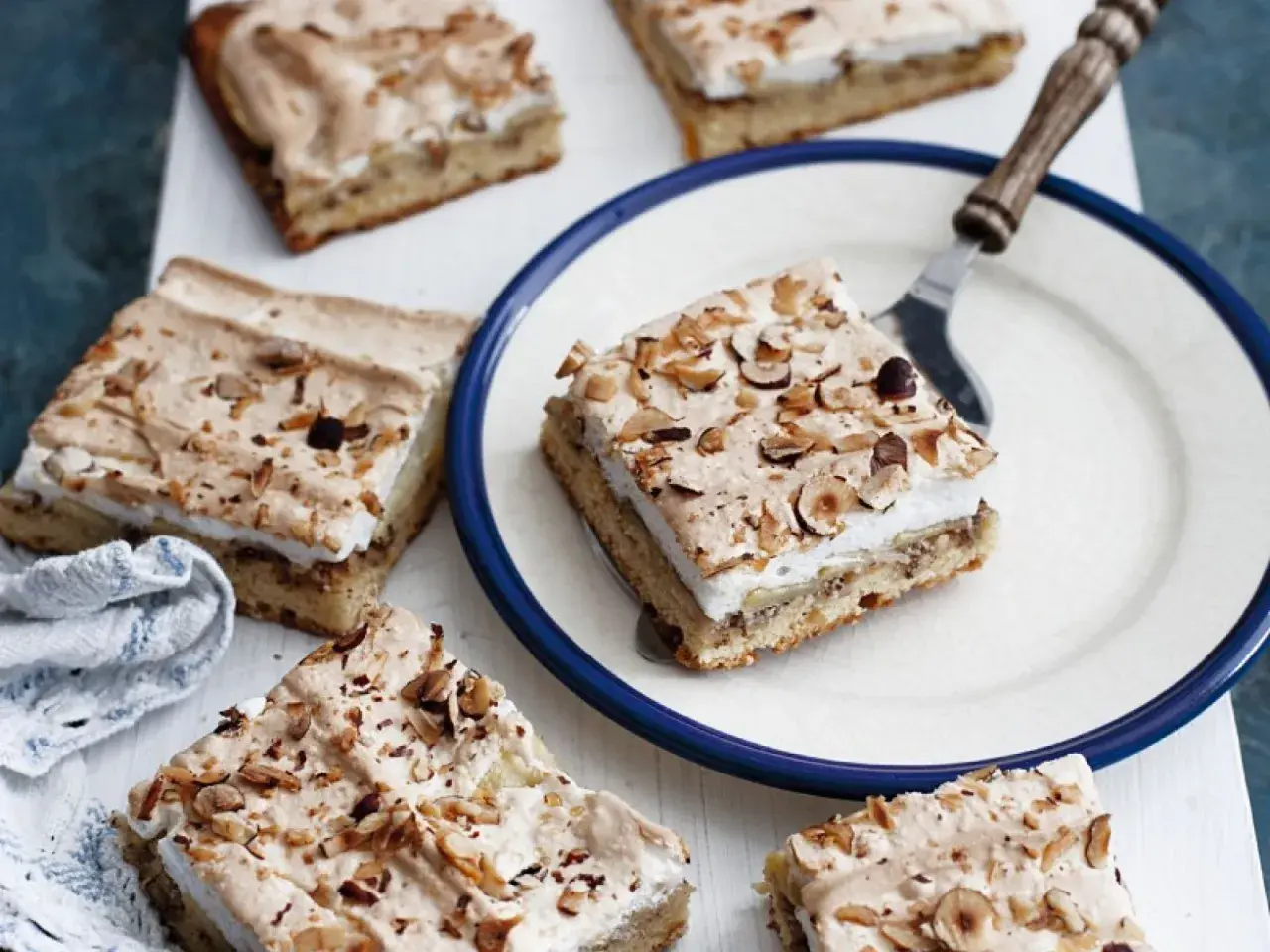 Saftiger Apfelkuchen mit Boskop-Äpfeln und Baiserhaube, bestreut mit gehackten Nüssen. Ein Stück auf einem Teller, bereit zum Genuss.