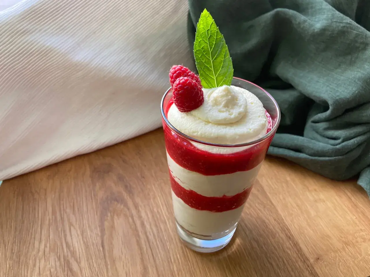 Schichtdessert im Glas mit Himbeersoße und einfacher Schmandcreme, garniert mit frischen Himbeeren und Minze.