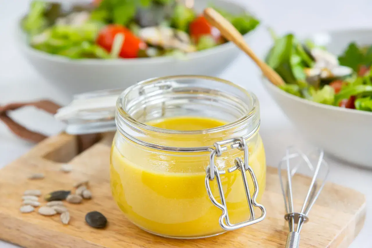 Frische, selbstgemachte Salatsauce im Glas, bereit für den Salat. Mit Kernen und einem kleinen Schneebesen daneben.
