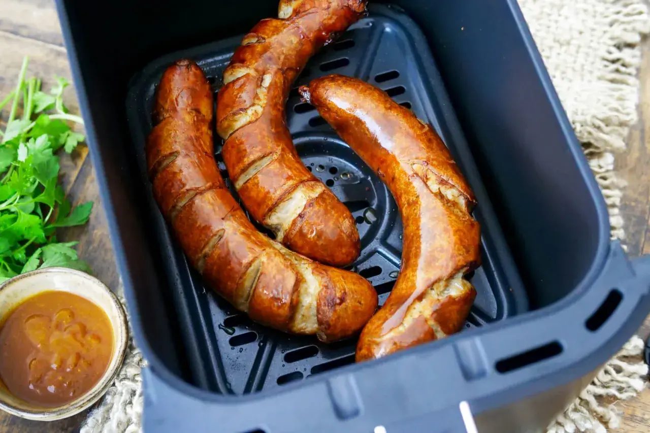 Drei goldbraune Bratwürste in der Friteuse, bereit zum Genießen. Daneben eine Schale mit Dip und frische Petersilie.