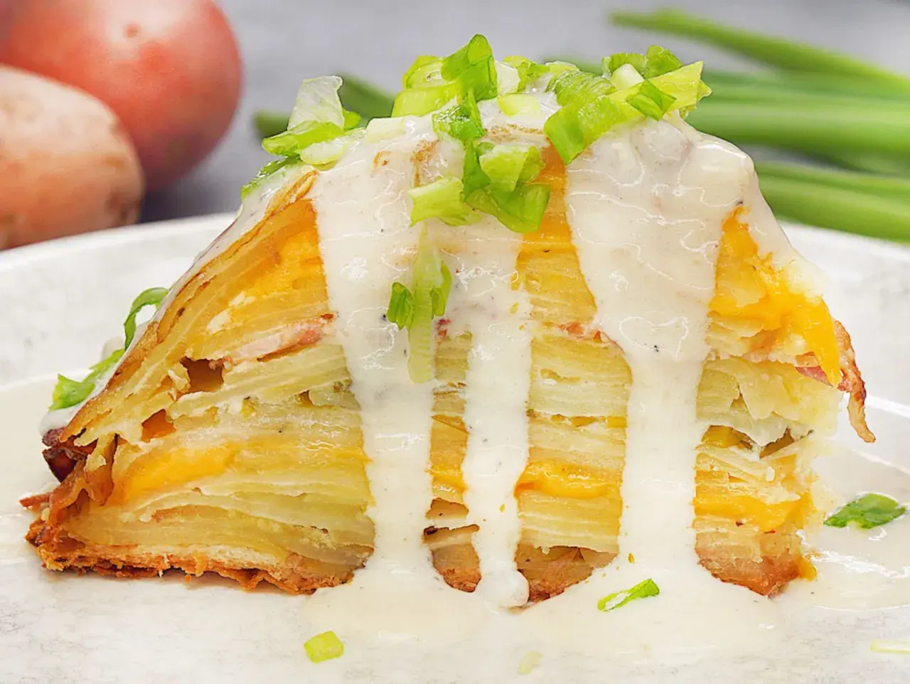 Ein Stück Kartoffelkuchen nach altem Rezept, geschichtet mit Käse und überzogen mit cremiger Sauce und Frühlingszwiebeln.