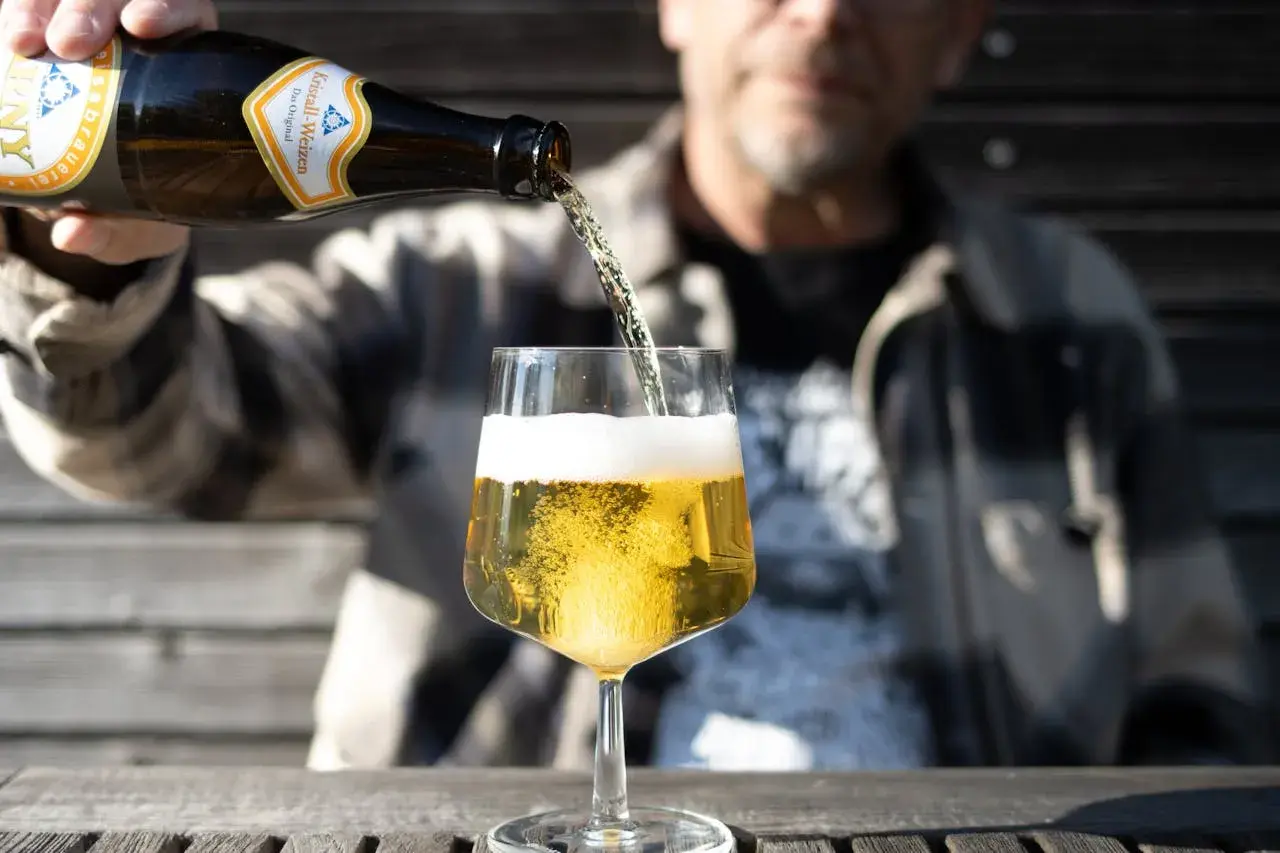 Mann schenkt helles Bier ein. Die Schaumkrone ist üppig. Wer auf Bier Kalorien achtet, wählt oft ein helles Weizen.