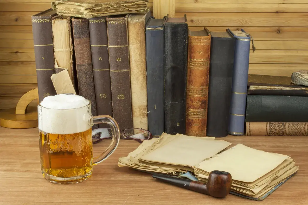 Ein Glas **Saison Bier** steht neben alten Büchern und einer Pfeife.