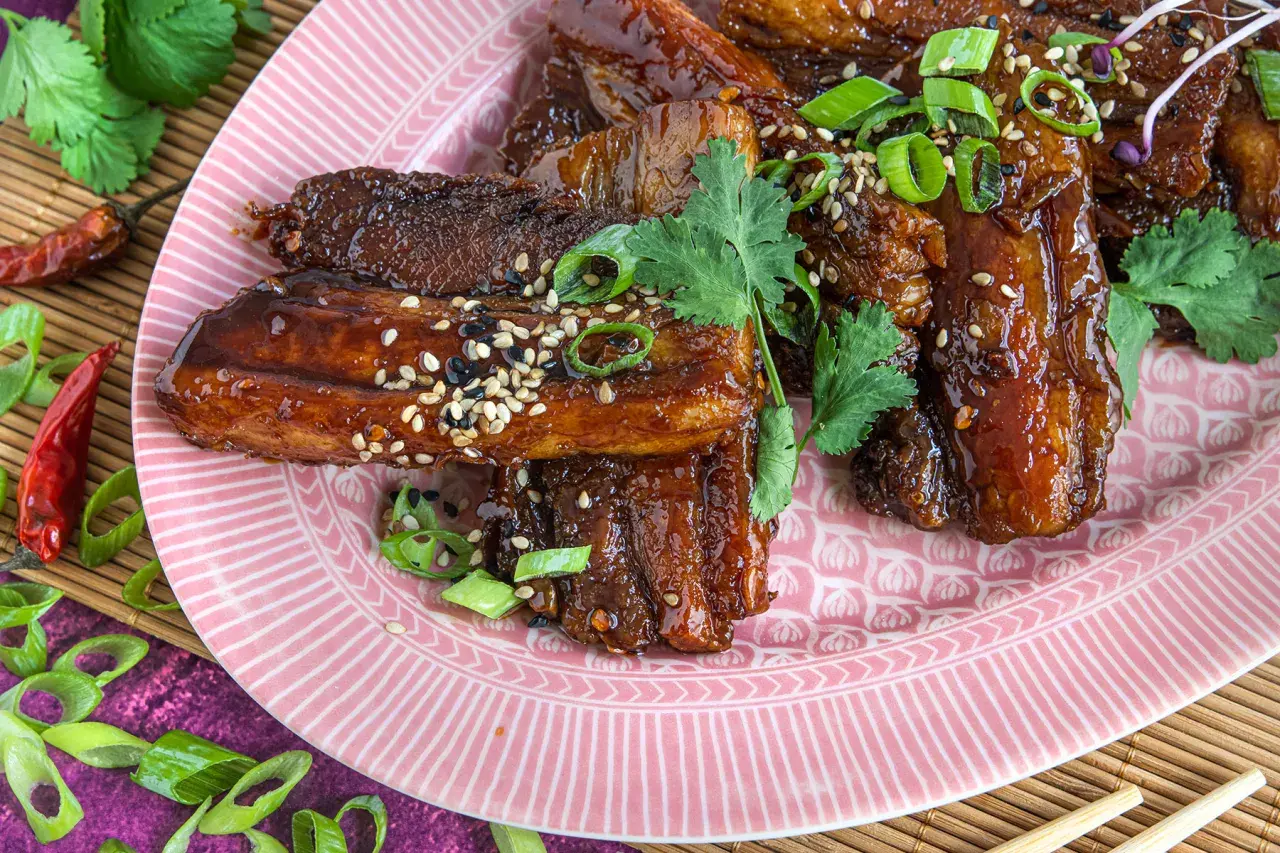 Glasierter schweinebauch asiatisch, garniert mit Frühlingszwiebeln und Sesam. Rote Chilischoten und Koriander runden das Gericht ab.