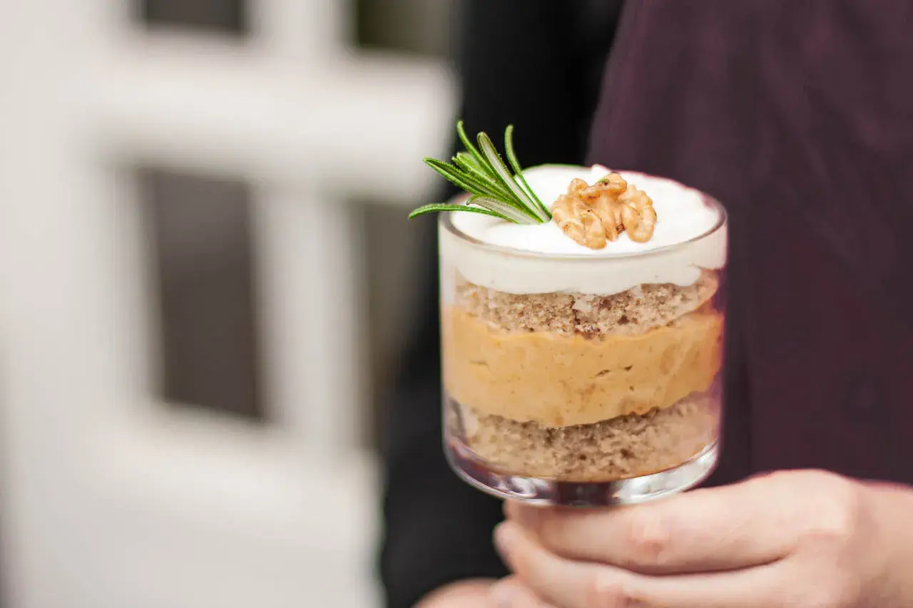 Ein Glas mit Schichten von Kuchen und cremiger Karamell-Mousse, garniert mit Rosmarin und einer Walnusshälfte.