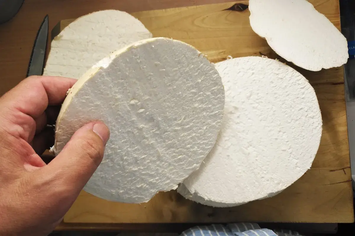 Ein Mensch hält eine dicke Scheibe eines riesigen Bovists, bereit für ein leckeres riesenbovist rezept. Mehrere weitere Scheiben liegen auf einem Holzbrett.
