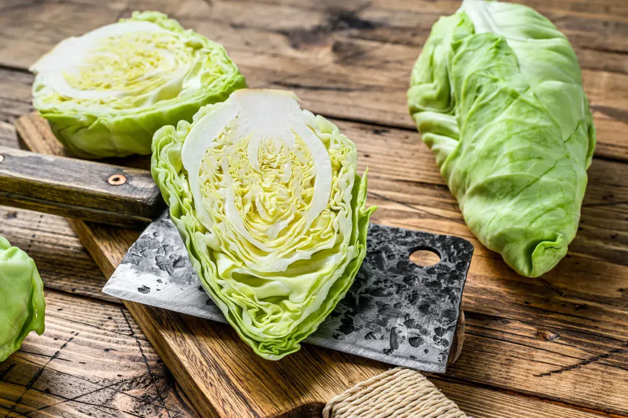 Frischer spitzkohl roh, halbiert und auf einem Holzbrett mit einem Hackmesser. Bereit für die Zubereitung eines knackigen Salats.
