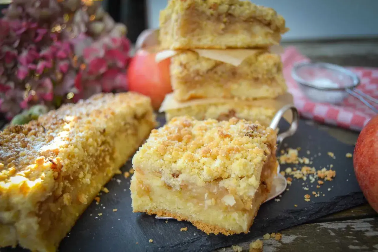 Omas weltbester Apfelkuchen: saftige Apfelschicht, knuspriger Streusel. Ein Stück Glück auf dunklem Schiefer.