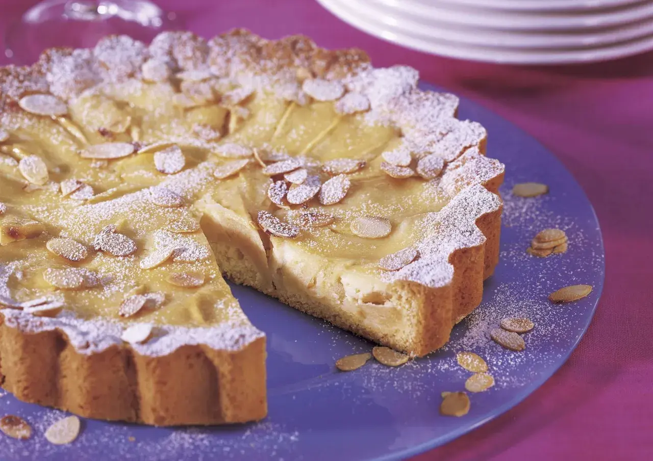 Ein köstlicher Apfelkuchen mit Guss, bestreut mit Puderzucker und Mandelblättchen, auf einem blauen Teller.