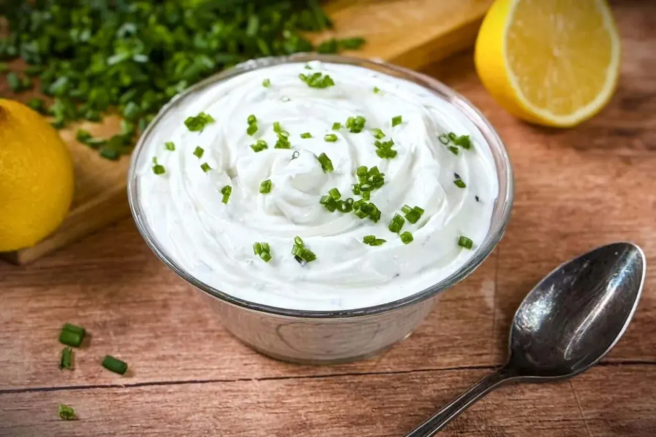 Cremige Sour Creme, frisch zubereitet, garniert mit Schnittlauch. Dazu Zitrone und ein Löffel. Perfekt zum Sour Creme selber machen.