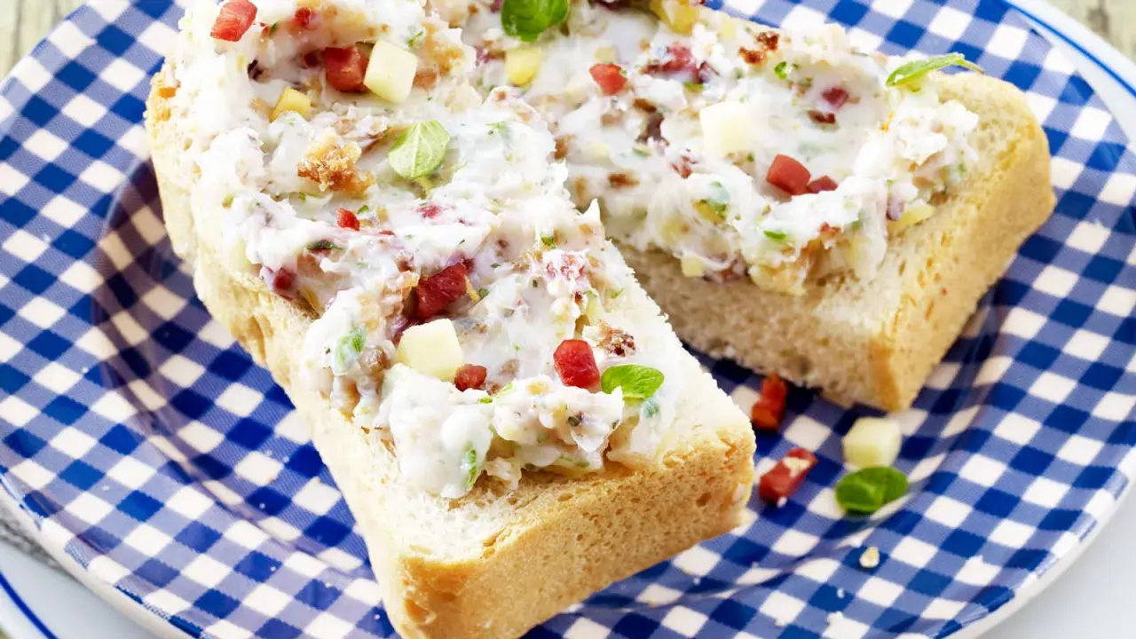 Schmalz-Brotaufstriche mit Speck und Kräutern auf rustikalem Brot, serviert auf blau-weiß karierter Platte.