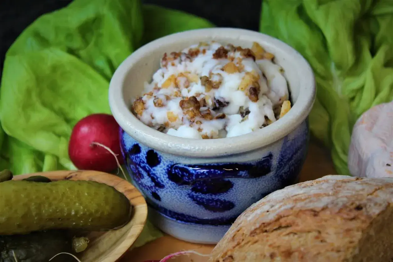 Griebenschmalz, ein traditionelles Gericht, in einem blauen Steingut-Napf, serviert mit Brot, Radieschen und Gewürzgurken.