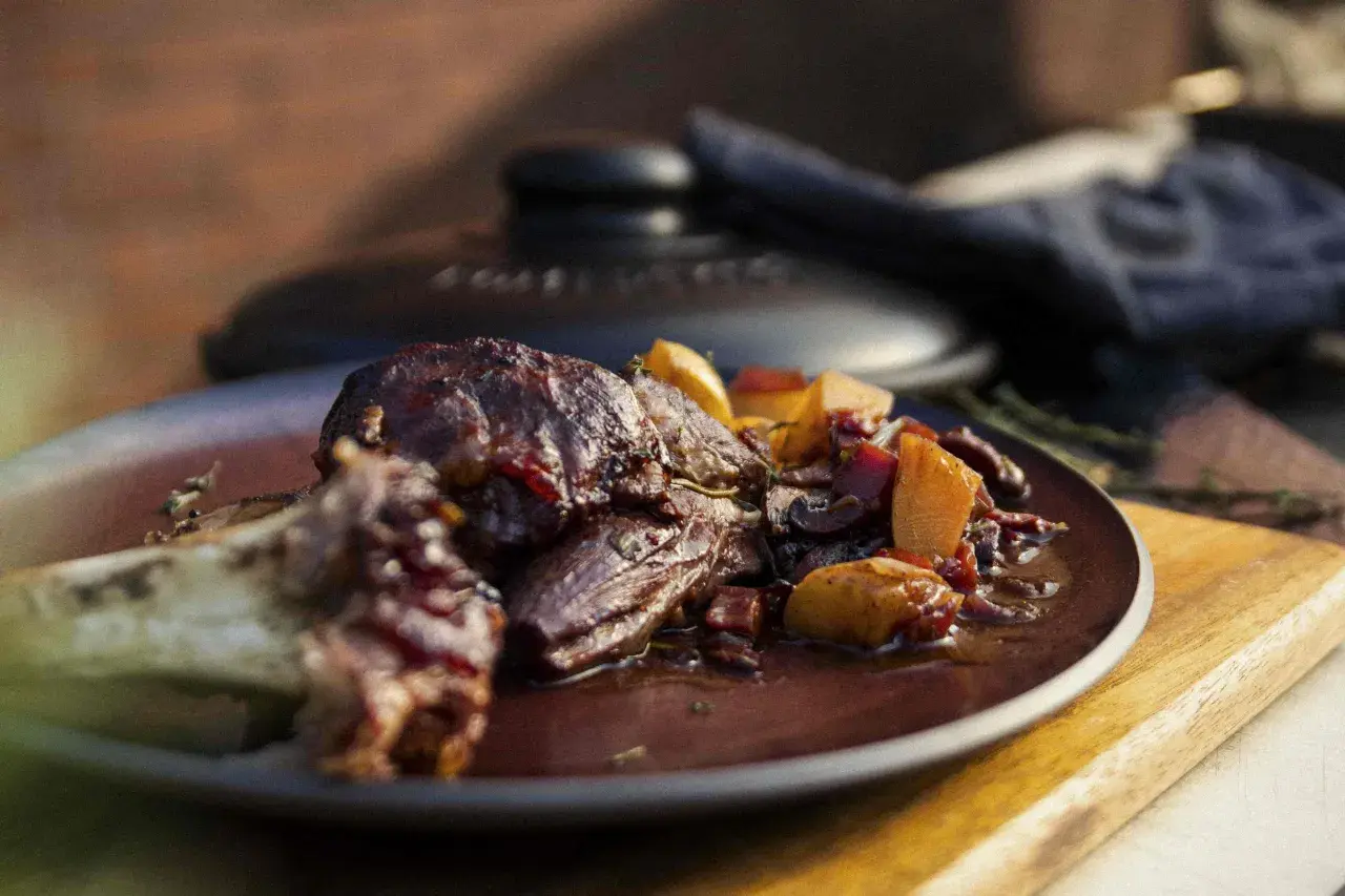 Ein saftiges Lammhaxe Rezept, serviert mit Wurzelgemüse in einer dunklen Sauce auf einem Teller.