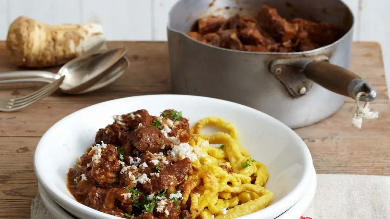 Herzhaftes Gulasch mit Spätzle, das Fleisch wurde perfekt mariniert. Daneben ein Meerrettich und Besteck.