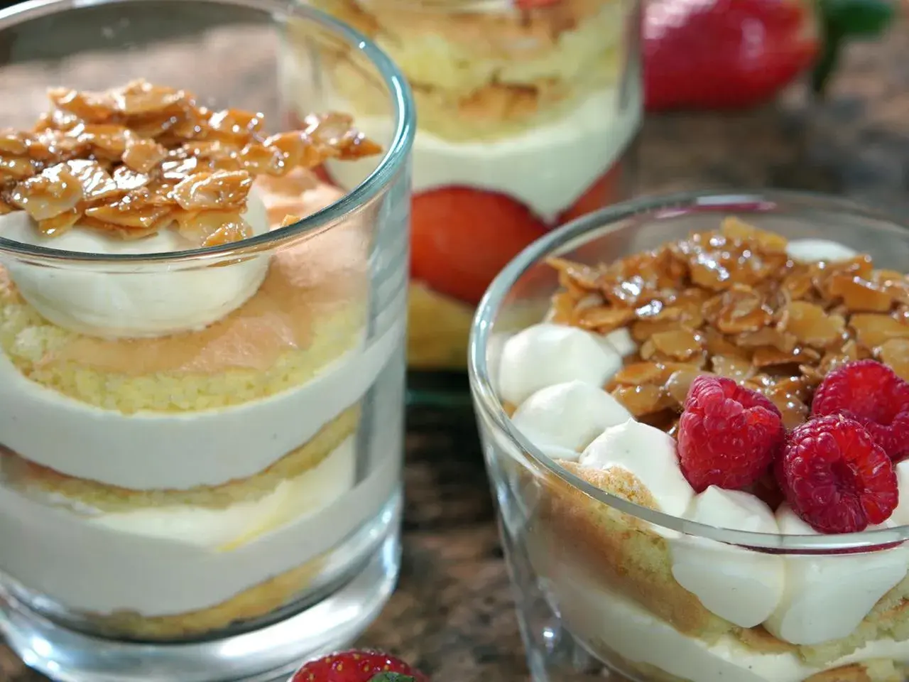 Schichten von Biskuit, Sahne und karamellisierten Mandeln, garniert mit Beeren. Ein köstlicher Bienenstich im Glas.