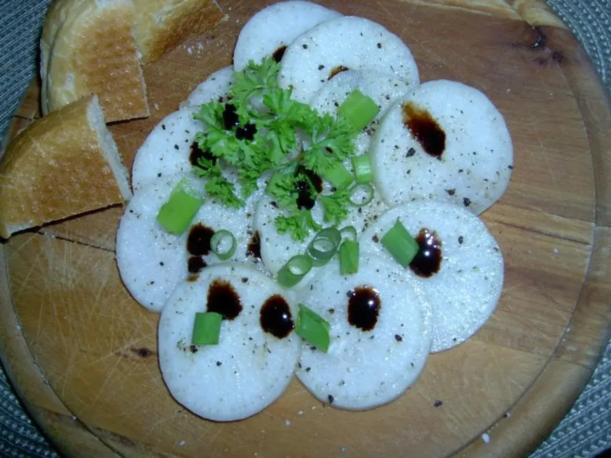 Frisch geschnittener Radi mit Kräutern und dunklem Balsamico auf Holzbrett, dazu Baguette.