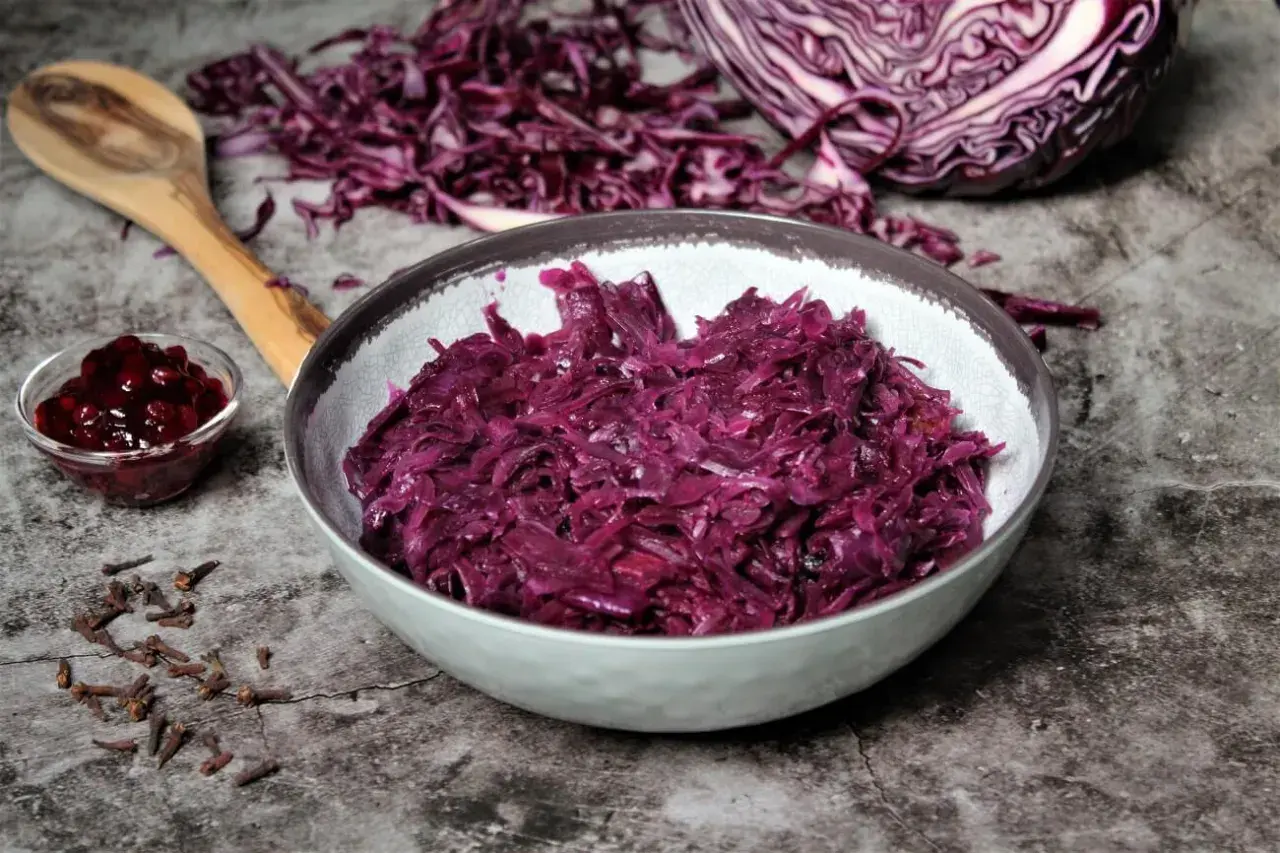 Schon probiert? Dieses rotkohl rezept einfach ist ein Genuss! Serviert in einer Schüssel, daneben ein Löffel, Gewürznelken und Preiselbeeren.