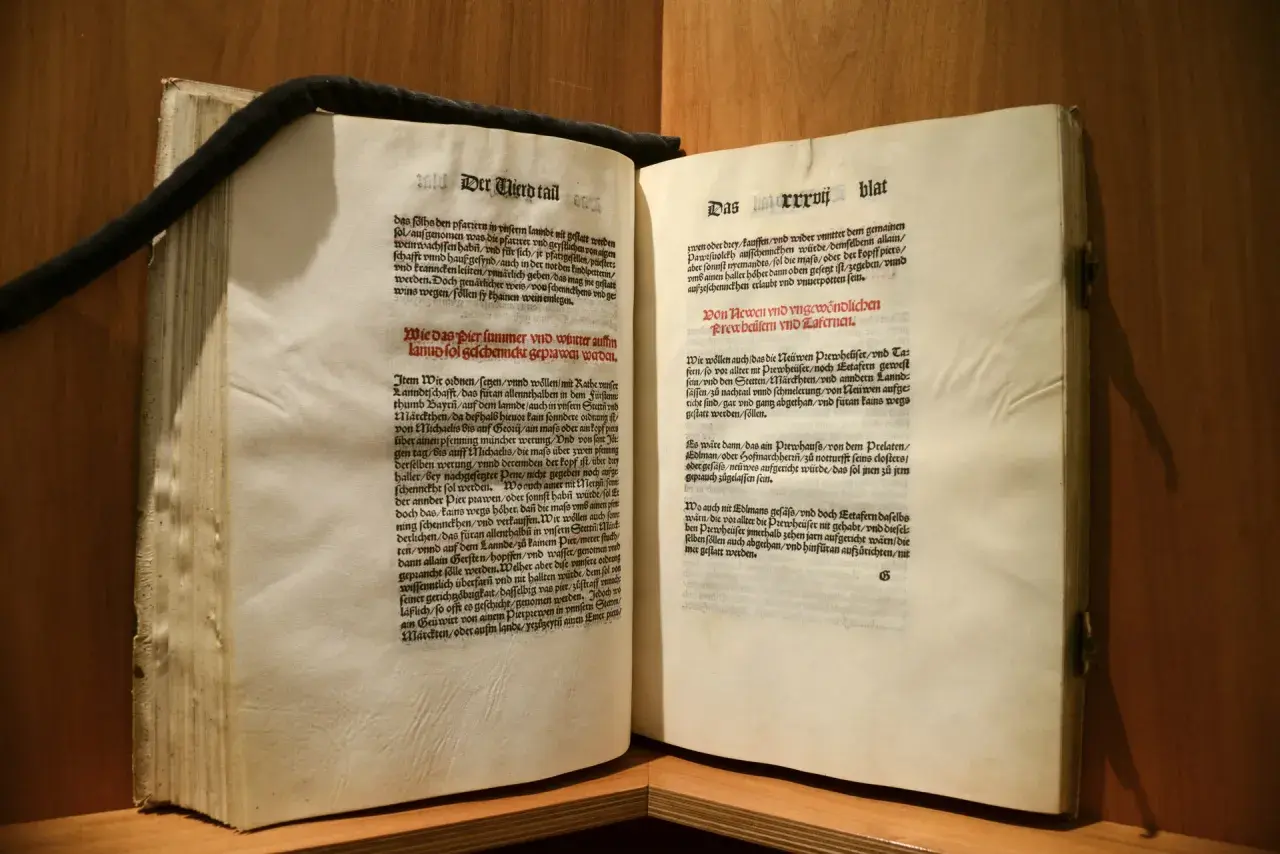 Altes Buch mit lateinischem Text. Ein schwarzes Band hält die Seiten zusammen. Das **deutsche Reinheitsgebot** von 1516 wird hier in alter Schrift zitiert.