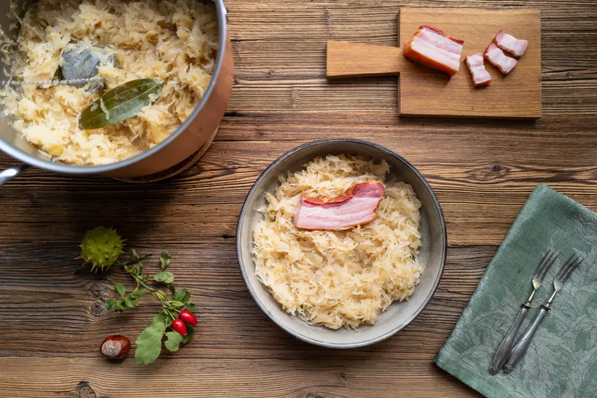 Herzhaftes Sauerkraut mit Speck, perfekt für ein Oktoberfest-Rezept. Ein Topf mit Sauerkraut und ein Teller mit dem fertigen Gericht stehen bereit.