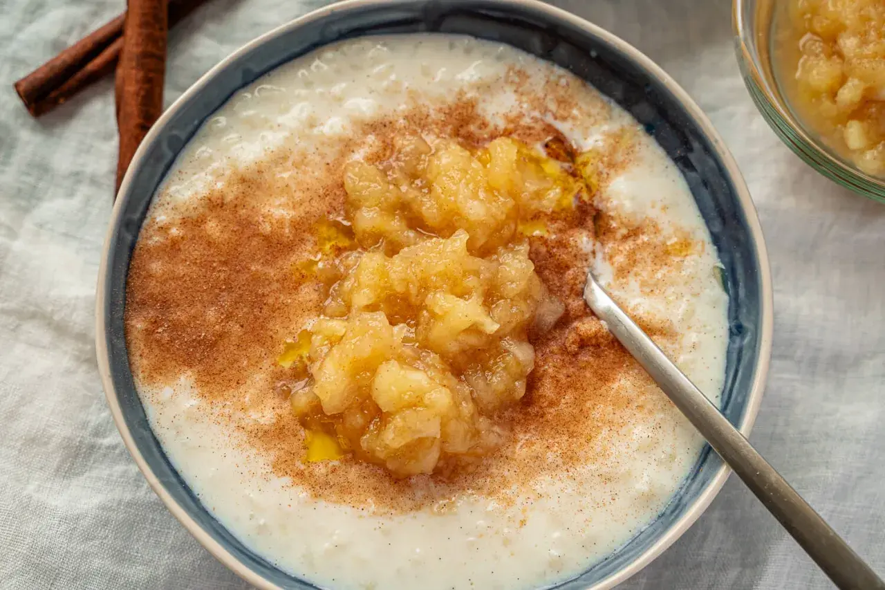 Cremiger Milchreis mit Apfelmus und Zimt, der weltbester Milchreis-Geschmack verspricht. Daneben liegen Zimtstangen.