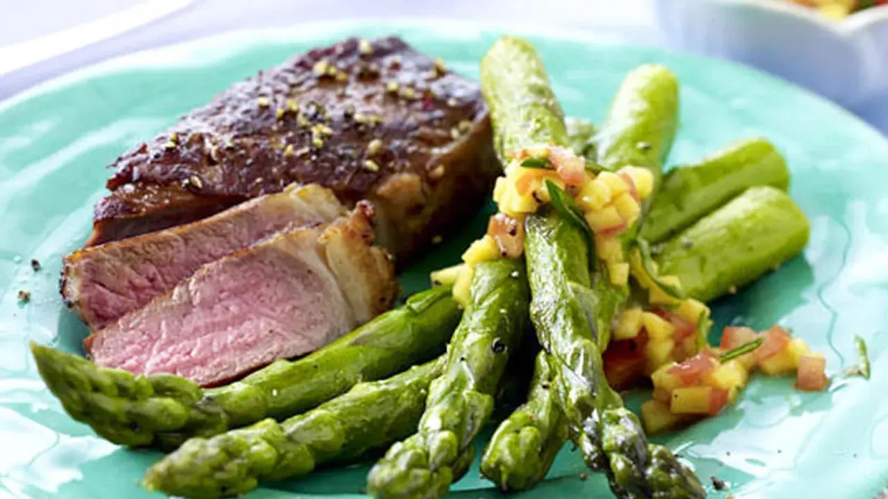 Saftiger Rumpsteak in der Pfanne, medium gebraten, serviert mit grünem Spargel und einer fruchtigen Salsa.
