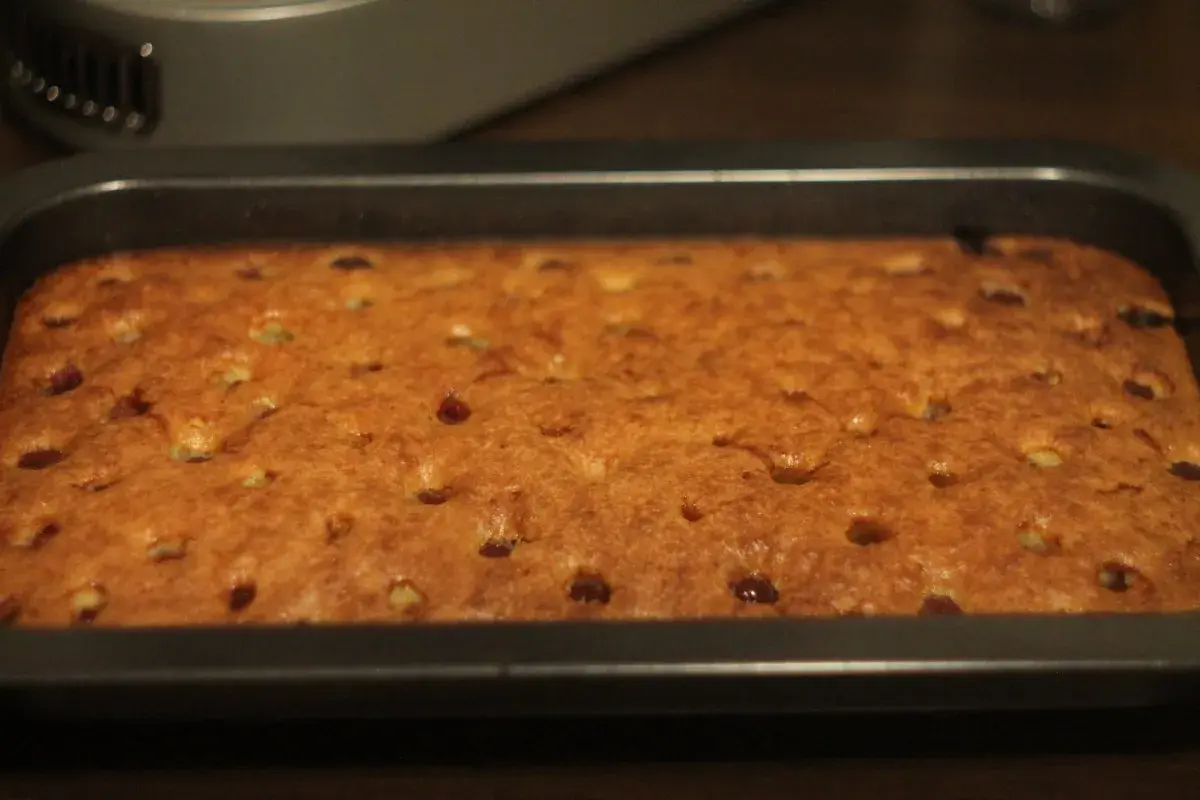Frisch gebackener, goldbrauner tante mathildas kirschkuchen in einer rechteckigen Backform. Kleine Kirschstücke sind im Teig verteilt.