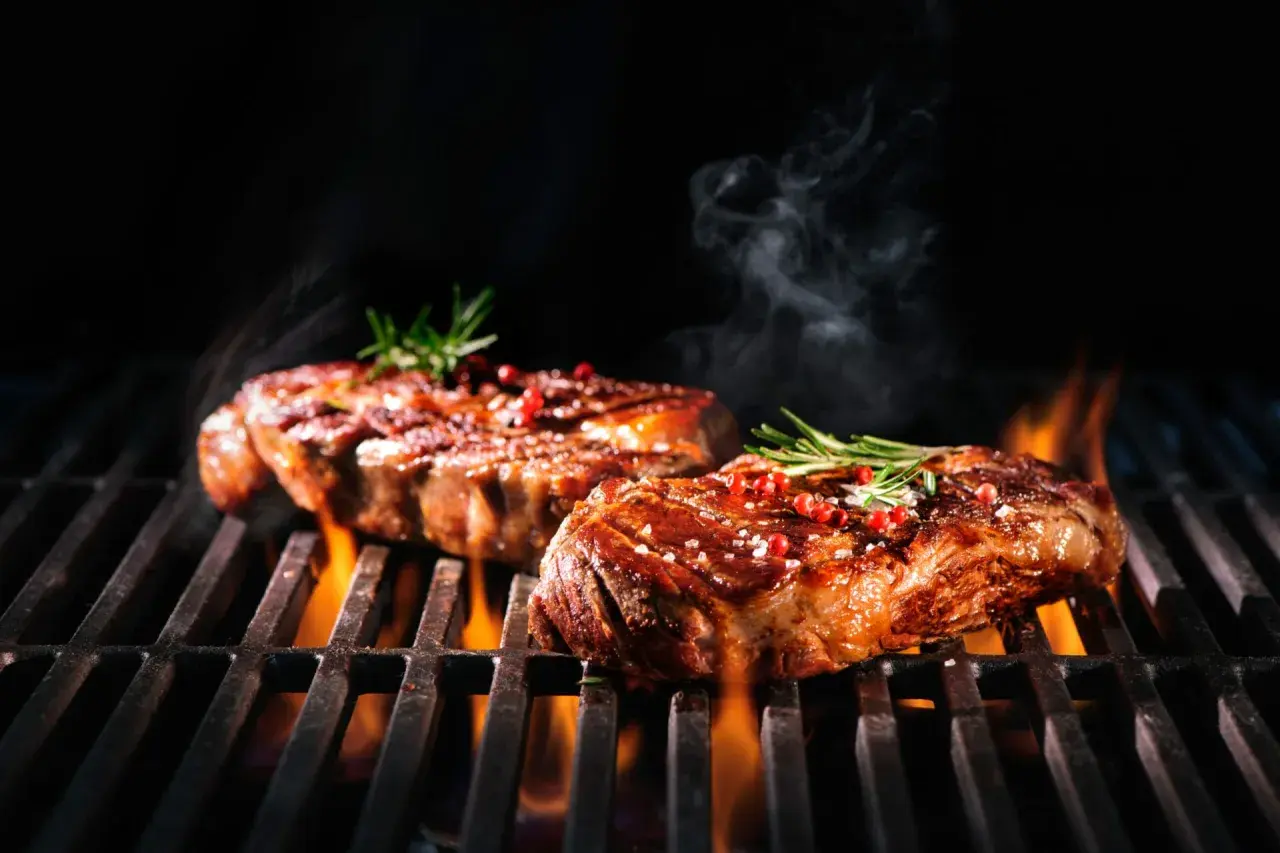 Zwei saftige Steaks brutzeln auf dem Grill, verfeinert mit einer Schwarzbier-Marinade, Rosmarin und rosa Pfeffer.