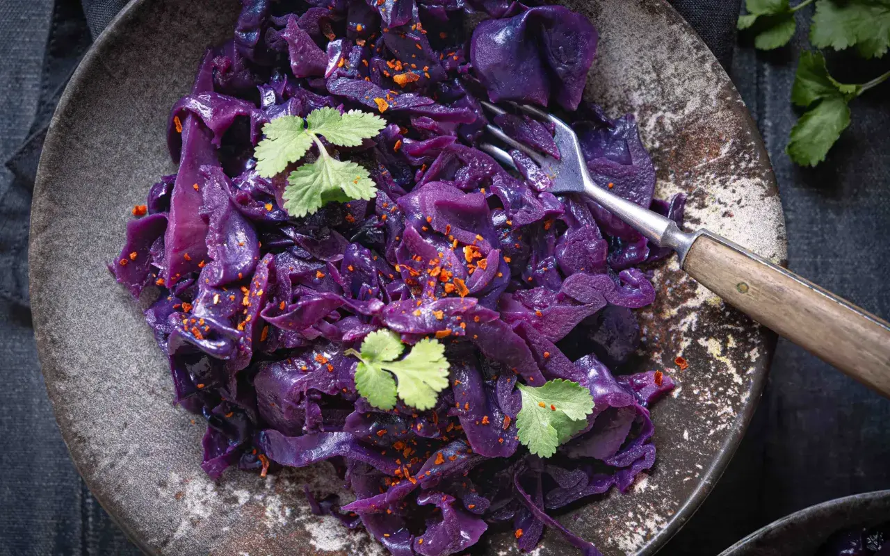 Ein Teller mit dampfendem rotkohl, verfeinert mit frischer Petersilie und Chili-Flocken. Eine Gabel ruht darin, bereit zum Genießen.