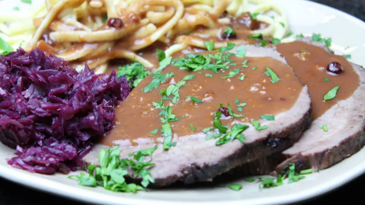 Sauerbraten einlegen rotwein: zarte Scheiben Fleisch in dunkler Soße, dazu Rotkohl und Nudeln.