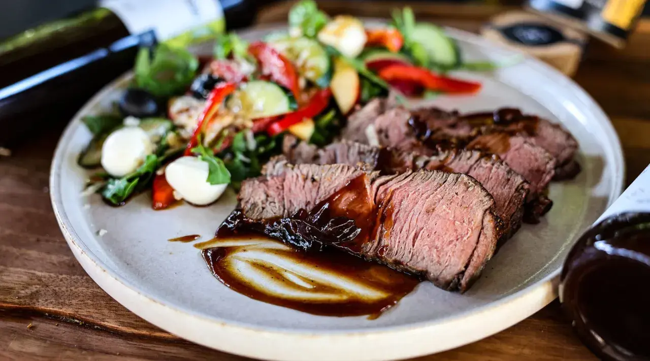 Saftiges Roastbeef als Beilage mit einem frischen Salat aus Tomaten, Gurken, Paprika und Mozzarella-Kugeln, beträufelt mit dunkler Sauce.