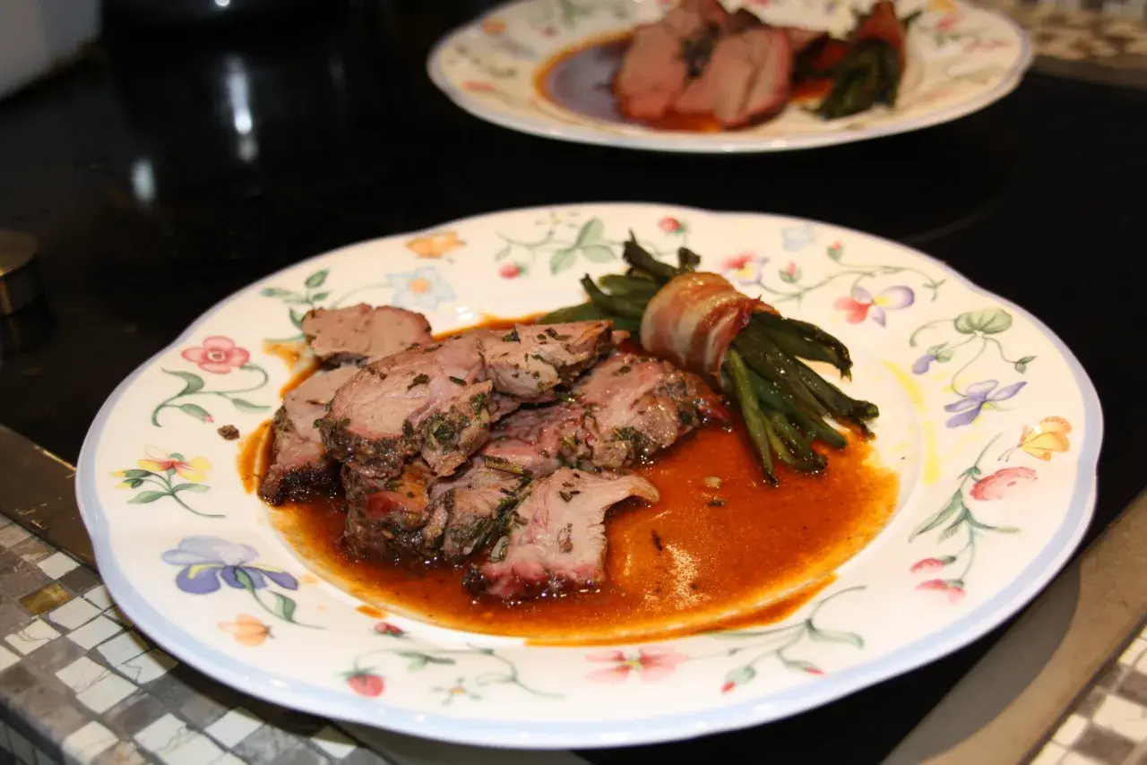 Zarte Lammfleischscheiben mit Kräutern, serviert mit Speck-umwickelten grünen Bohnen und einer köstlichen Sauce zu Lamm.