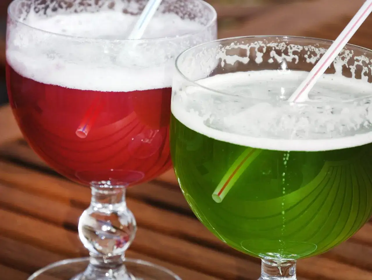 Zwei Gl&auml;ser mit schaumigen Berliner Weisse Sorten, rot und gr&uuml;n, mit Strohhalmen, auf Holztisch.