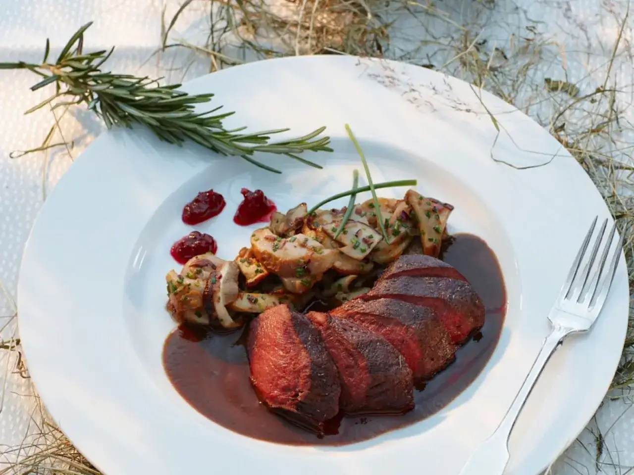 Ein k&ouml;stliches Rehhals-Rezept: Zartes Rehfleisch mit Pilzen, Preiselbeeren und einer kr&auml;ftigen Sauce auf einem wei&szlig;en Teller.