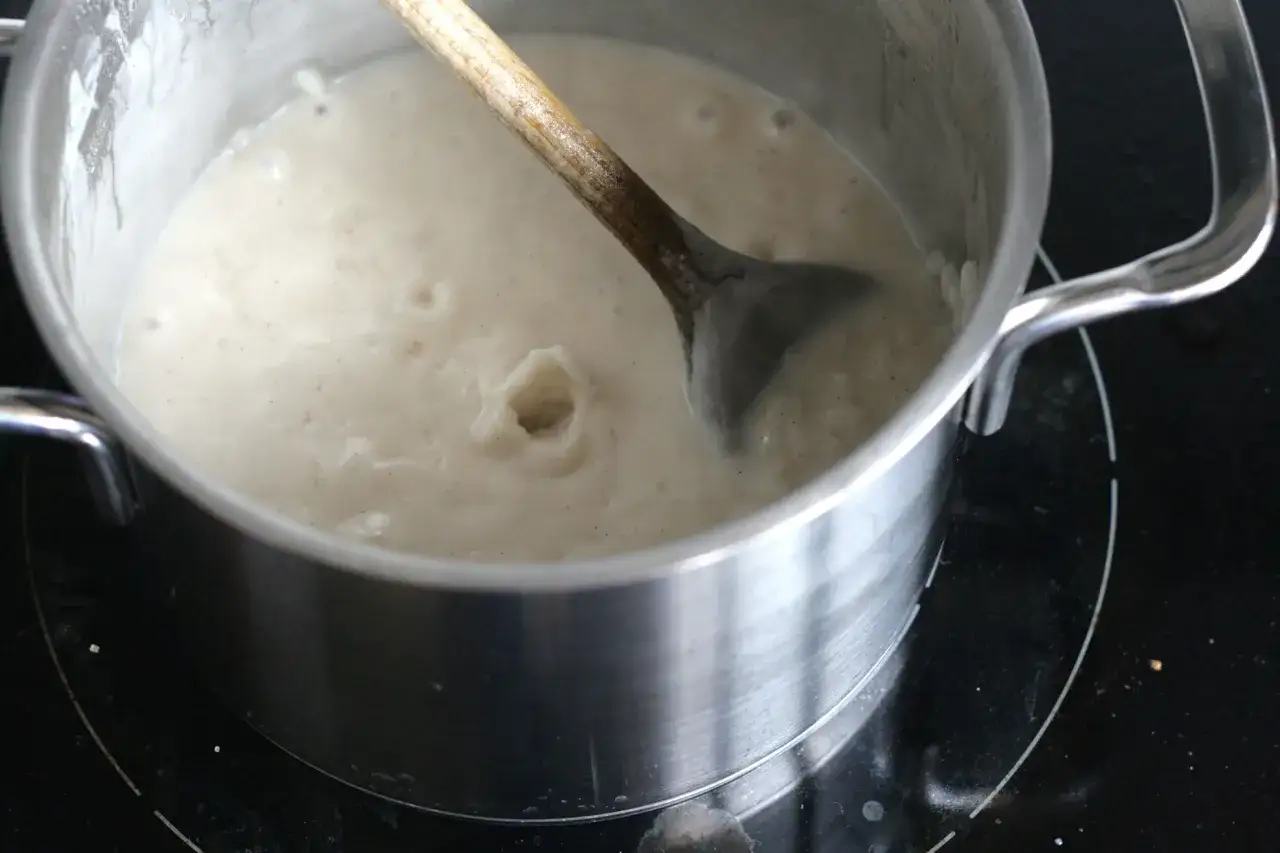 Ein Holzl&ouml;ffel r&uuml;hrt in einem Topf mit cremigem Milchreis, der gerade k&ouml;chelt. Dieser weltbester Milchreis wird sicher k&ouml;stlich!