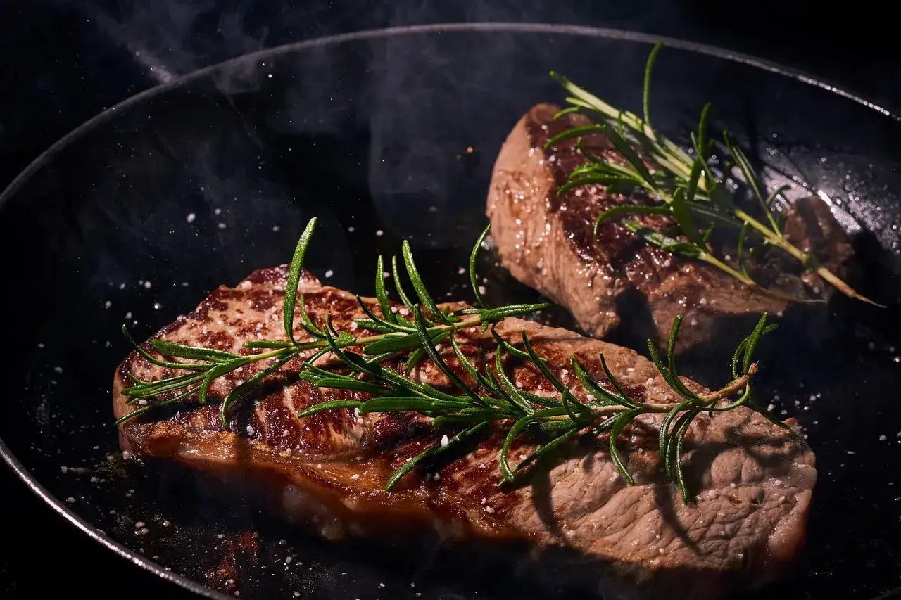 Zwei saftige Rumpsteaks brutzeln in der Pfanne, garniert mit frischem Rosmarin und grobem Salz. Dampf steigt auf und verhei&szlig;t ein k&ouml;stliches Mahl.