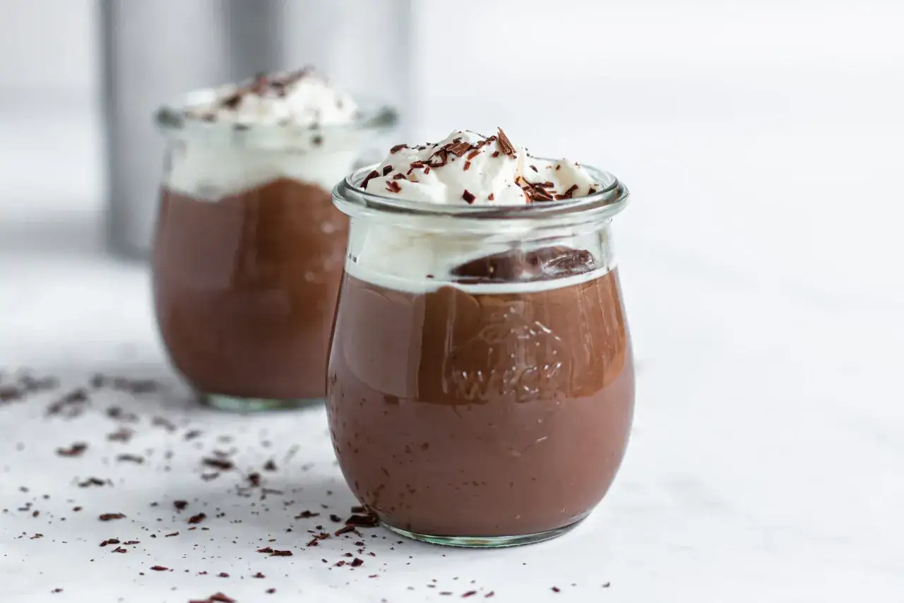 Zwei Gl&auml;ser mit cremigem Schokopudding, gekr&ouml;nt mit Schlagsahne und Schokostreuseln. Perfekt, um Schokopudding selber machen mit Kakao zu genie&szlig;en.