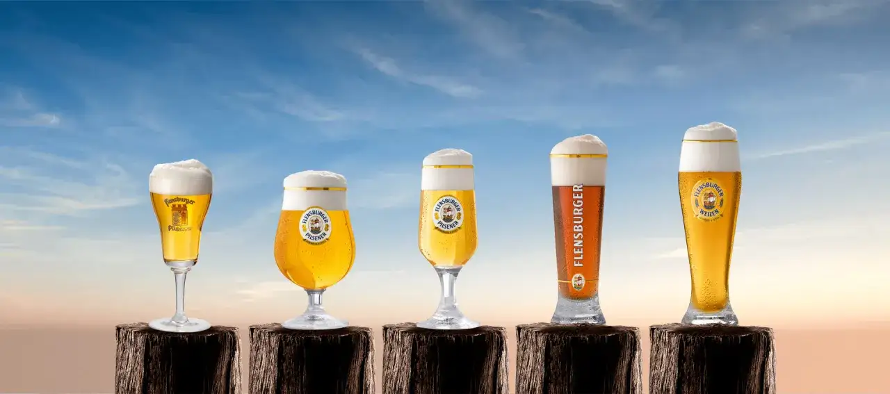 F&uuml;nf Gl&auml;ser mit Flensburger Bier stehen nebeneinander. Ein Bier Vergleich der verschiedenen Sorten unter blauem Himmel.