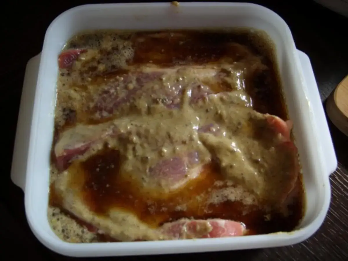 Fleischst&uuml;cke in einer wei&szlig;en Schale, bedeckt mit einer dunklen, schaumigen schwarzbier marinade.