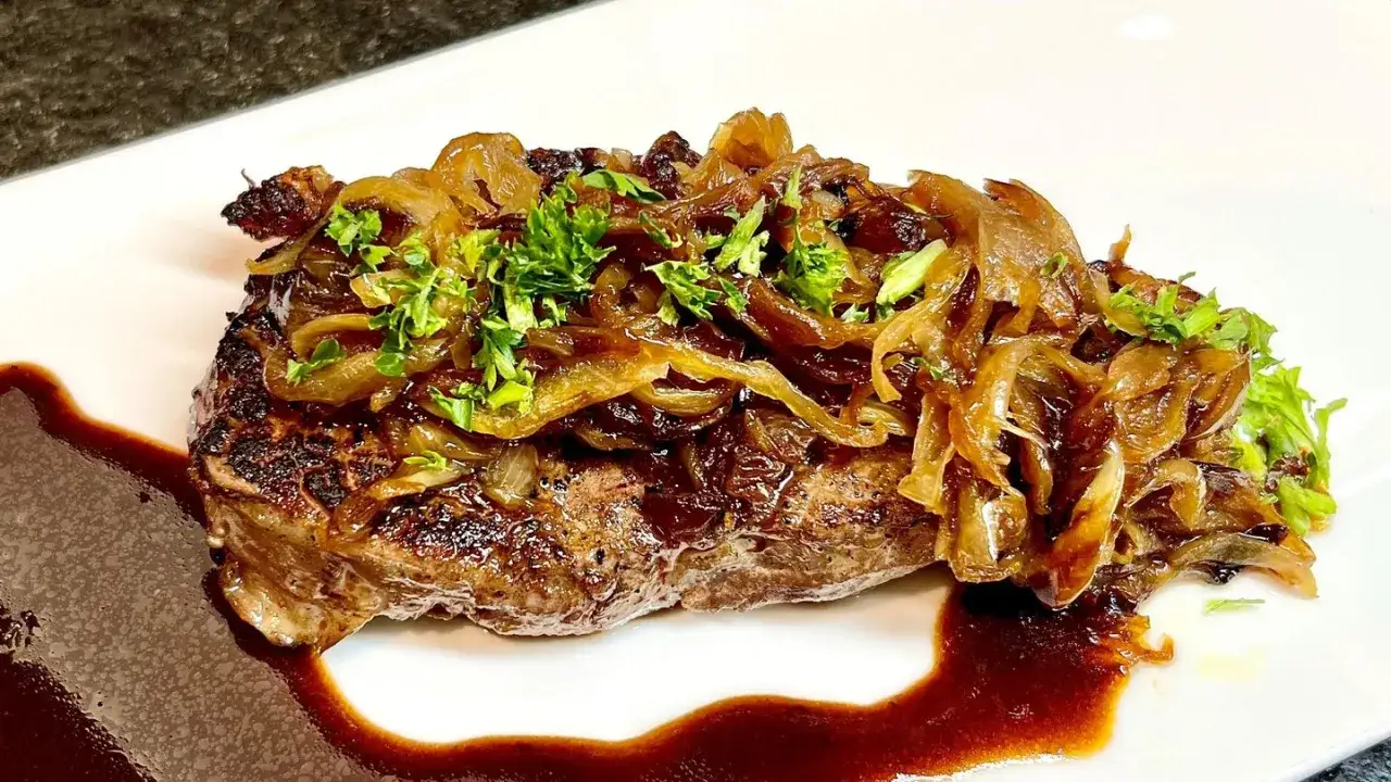 Saftiger Rostbraten, zubereitet im Backofen, mit karamellisierten Zwiebeln und frischer Petersilie garniert, serviert mit einer dunklen Sauce.