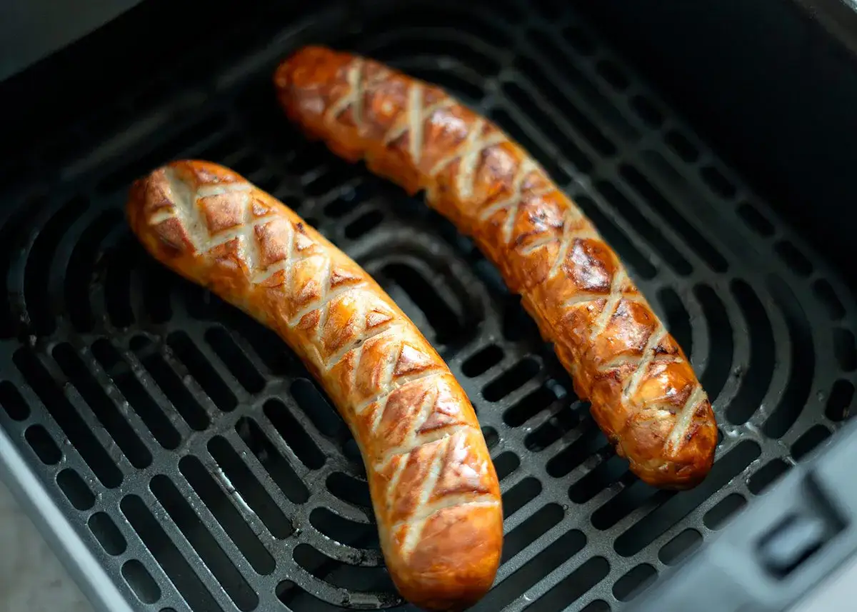 Zwei goldbraune Bratwürste mit Rautenmuster liegen auf dem Rost einer Heißluftfritteuse und werden knusprig.