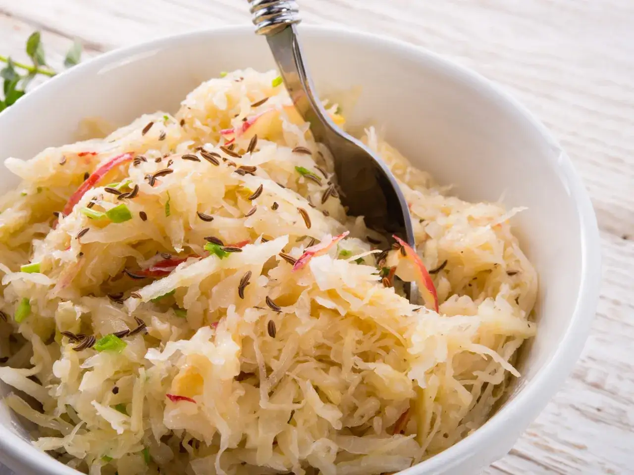 Schon probiert, wie man Sauerkraut aus dem Glas zubereiten kann? Hier ist ein k&ouml;stlicher, hausgemachter Sauerkraut-Salat mit K&uuml;mmel und Apfelst&uuml;cken, serviert in einer wei&szlig;en Sch&uuml;ssel.