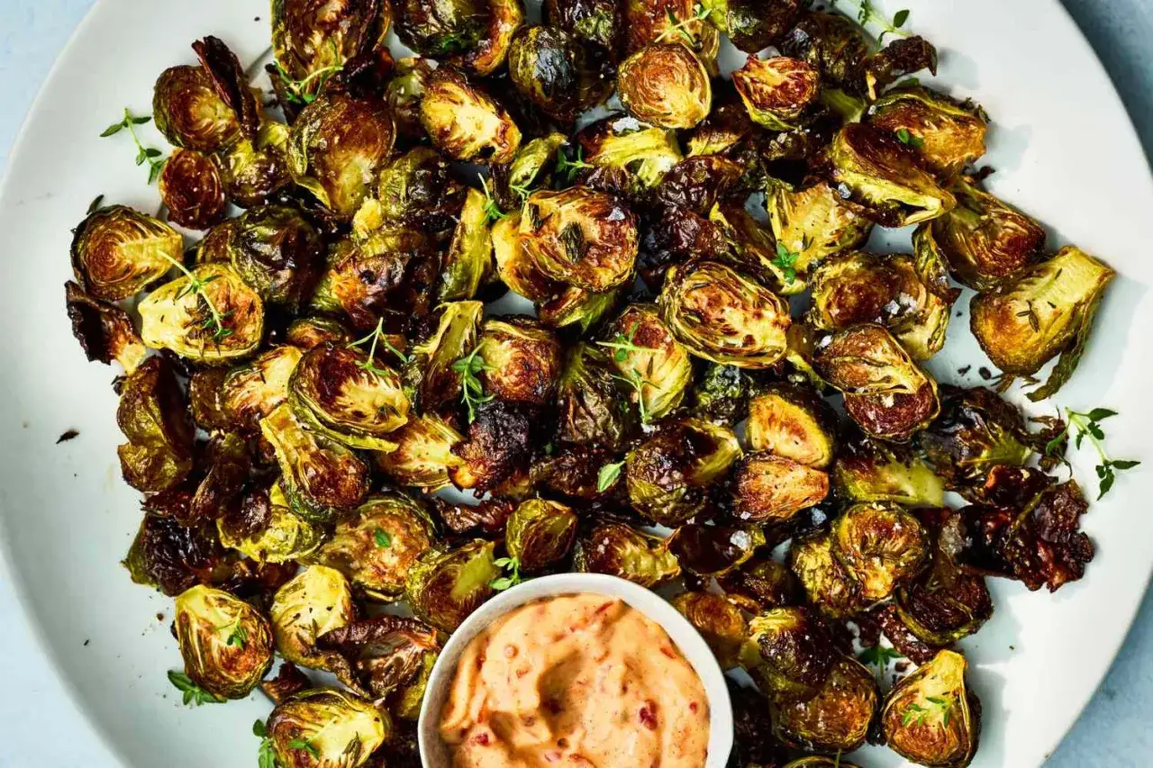 Knusprig gebratenen Rosenkohl mit Kr&auml;utern und einer cremigen Dip-Sauce auf einem Teller.