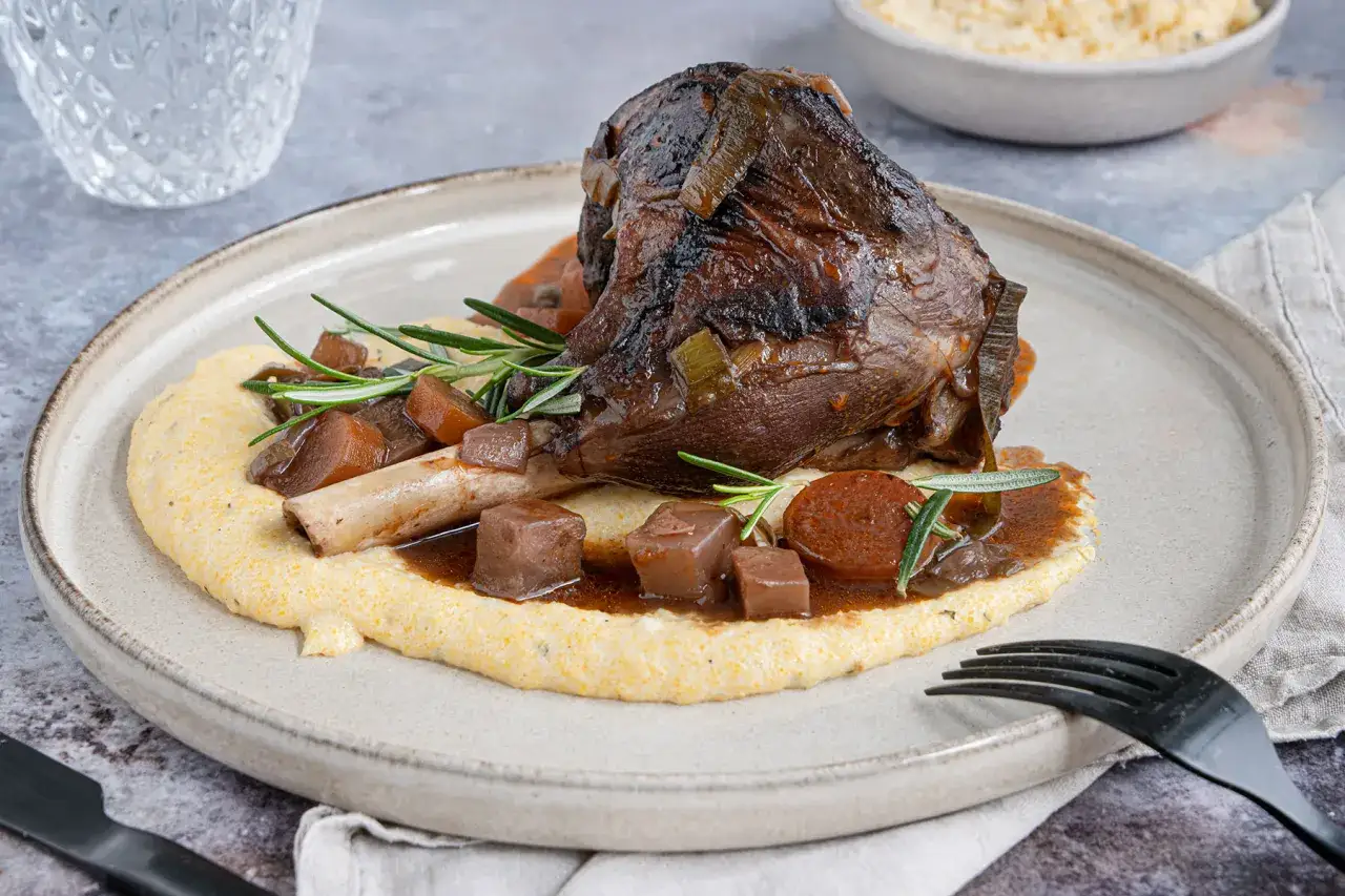 Ein zartes Lammhaxe Rezept auf cremigem Polenta, garniert mit Rosmarin und karamellisierten Zwiebeln.